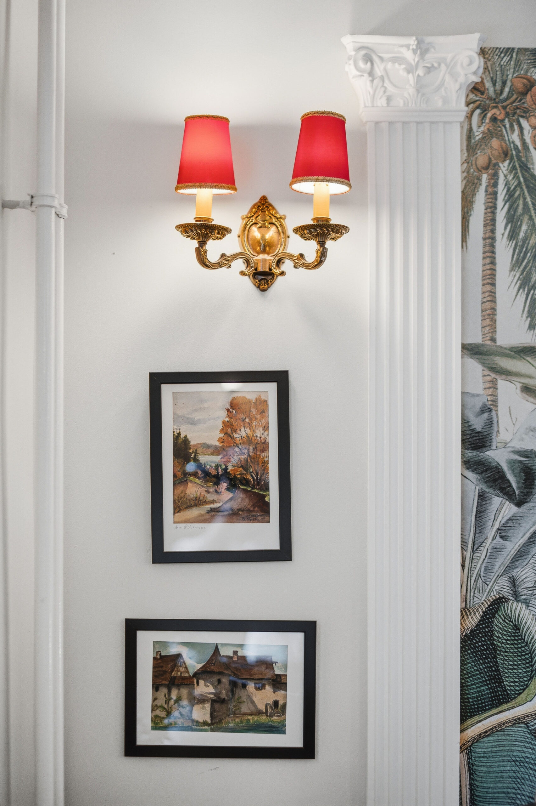 Wall sconce with red shades above framed pictures