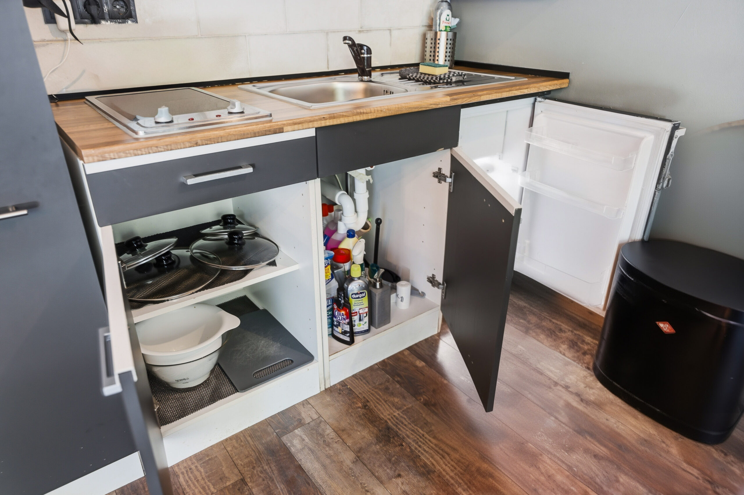 Kitchen sink area with open cabinet and supplies