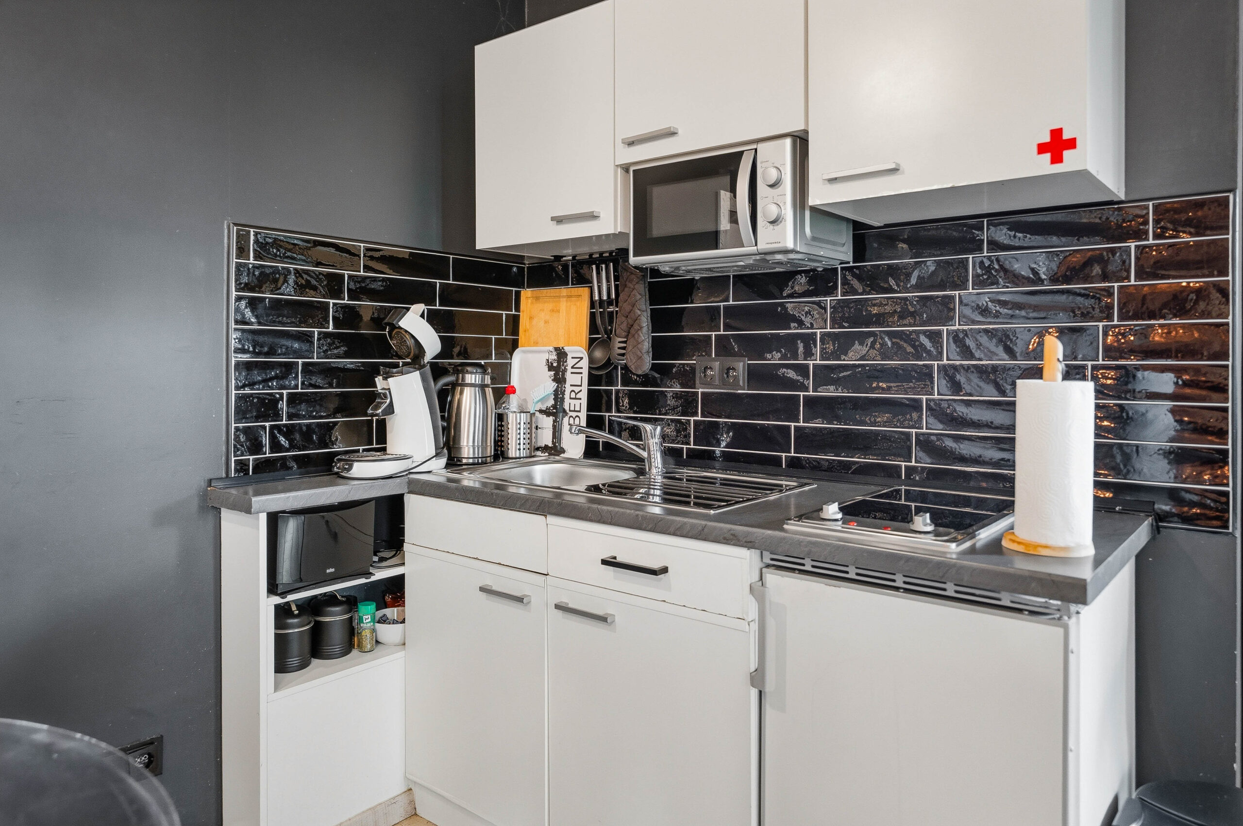 Compact kitchen with white cabinets and black tile backsplash