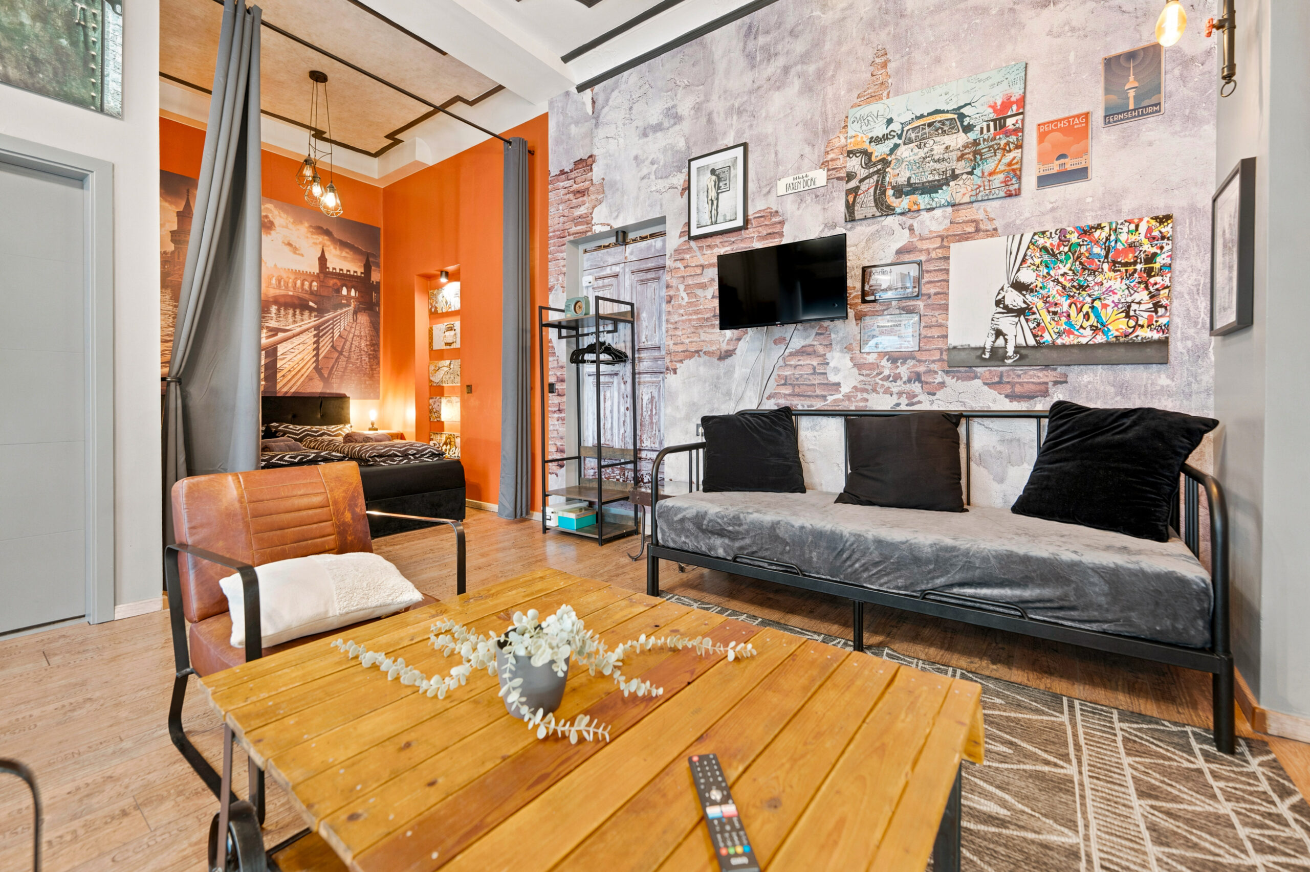 Studio layout with orange accent wall, bed, sofa, kitchen