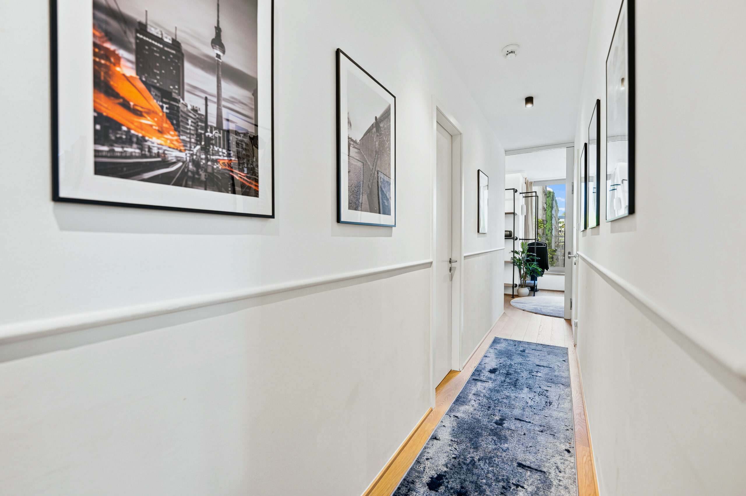 Long hallway with framed pictures and blue runner rug