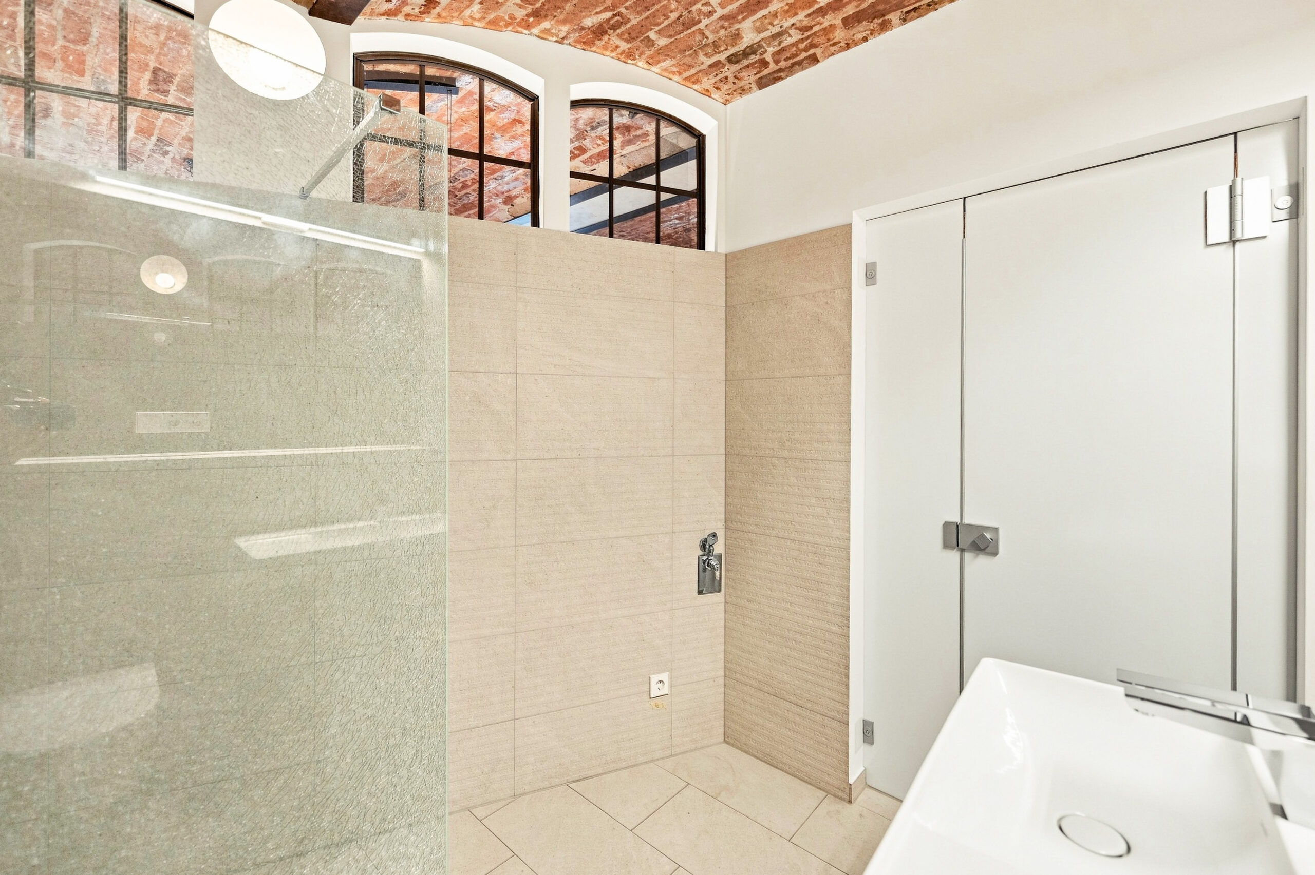 Bright bathroom with walk-in shower, cream tiles, and exposed brick