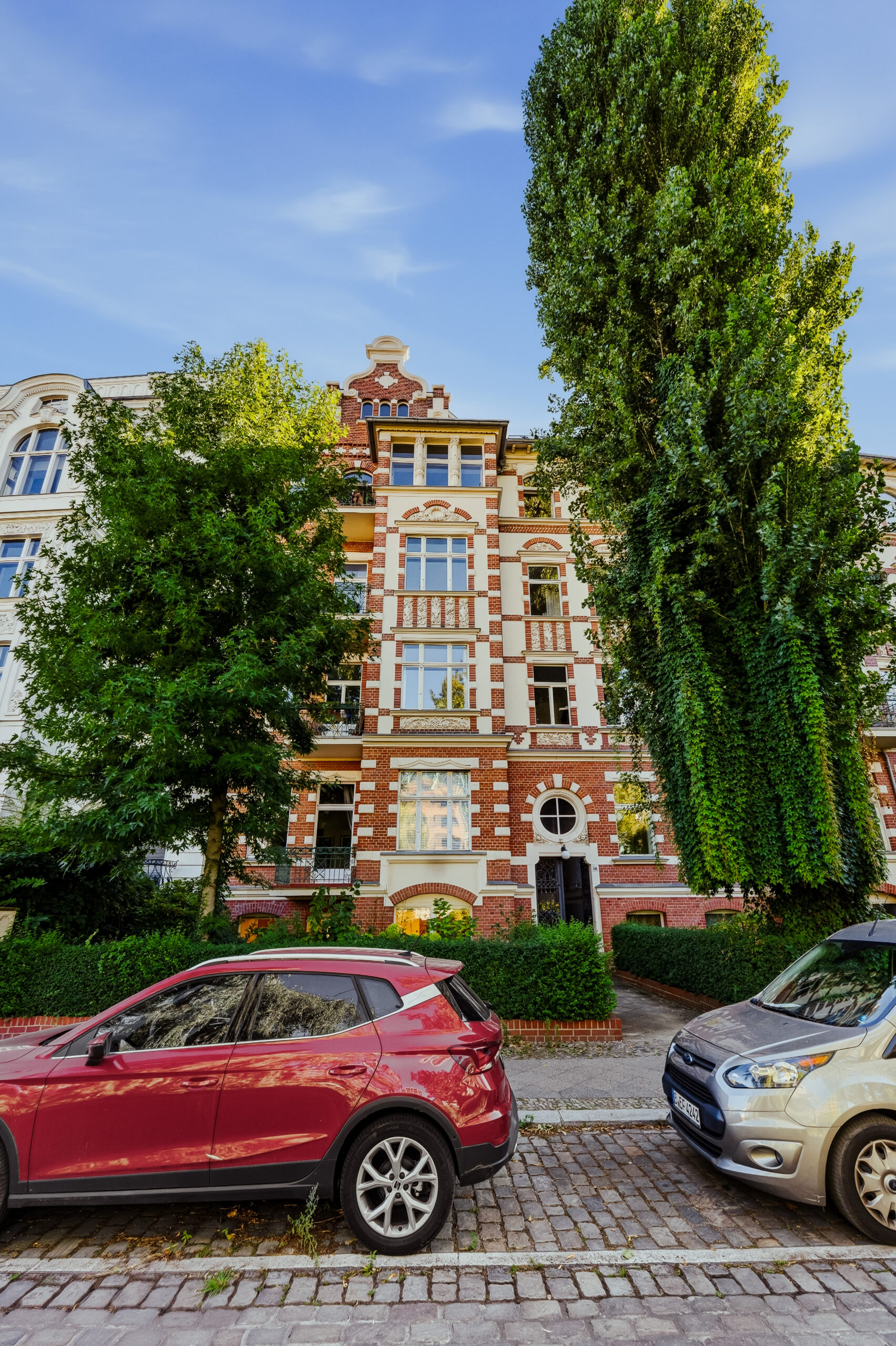 Red brick period building with parked cars and tall cypress trees