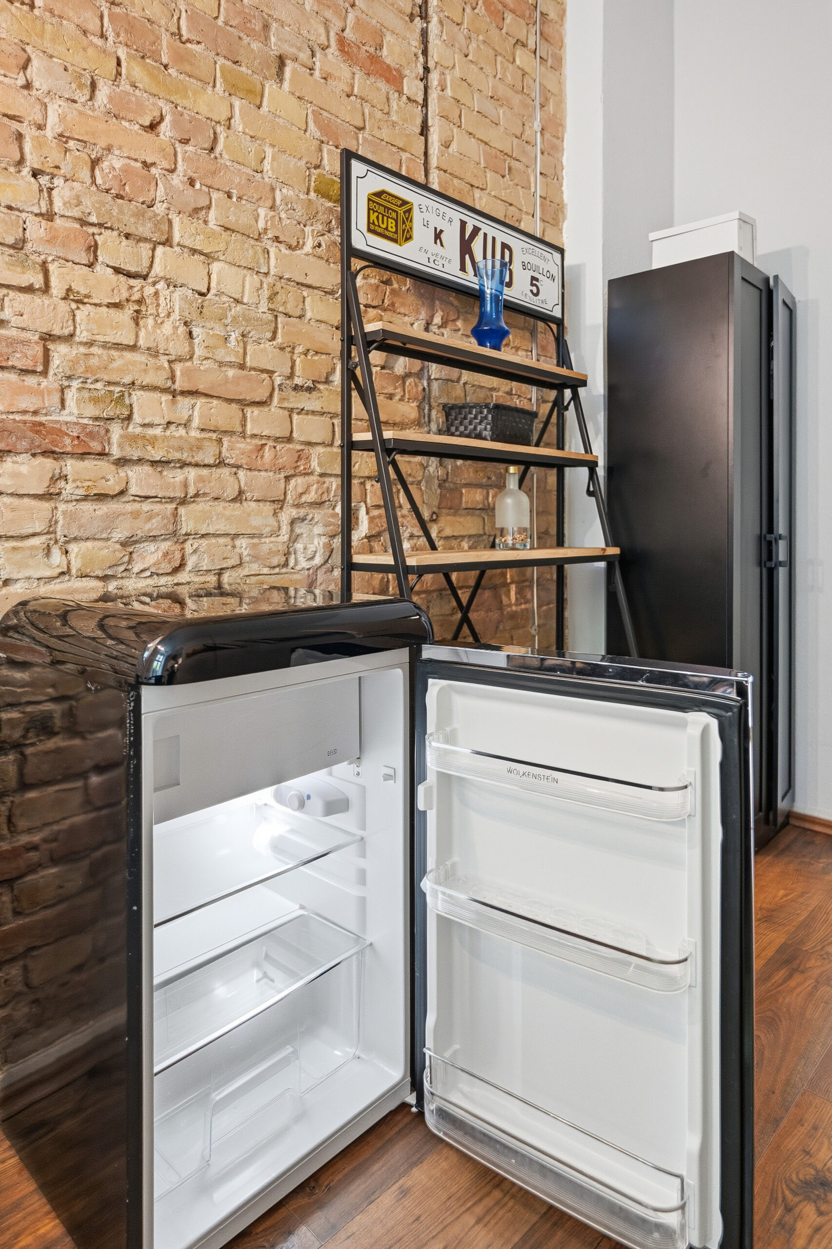 Open empty refrigerator near brick wall