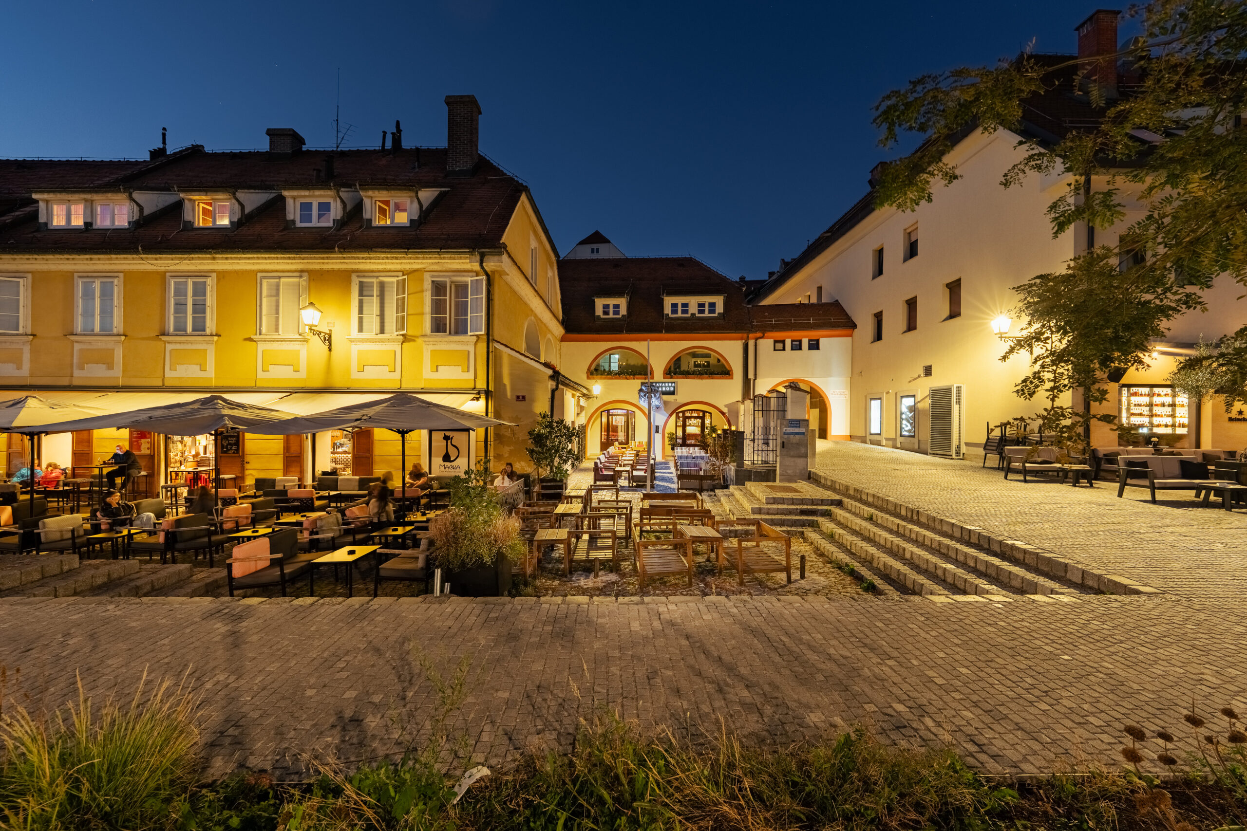 Illuminated courtyard with steps and outdoor tables at night