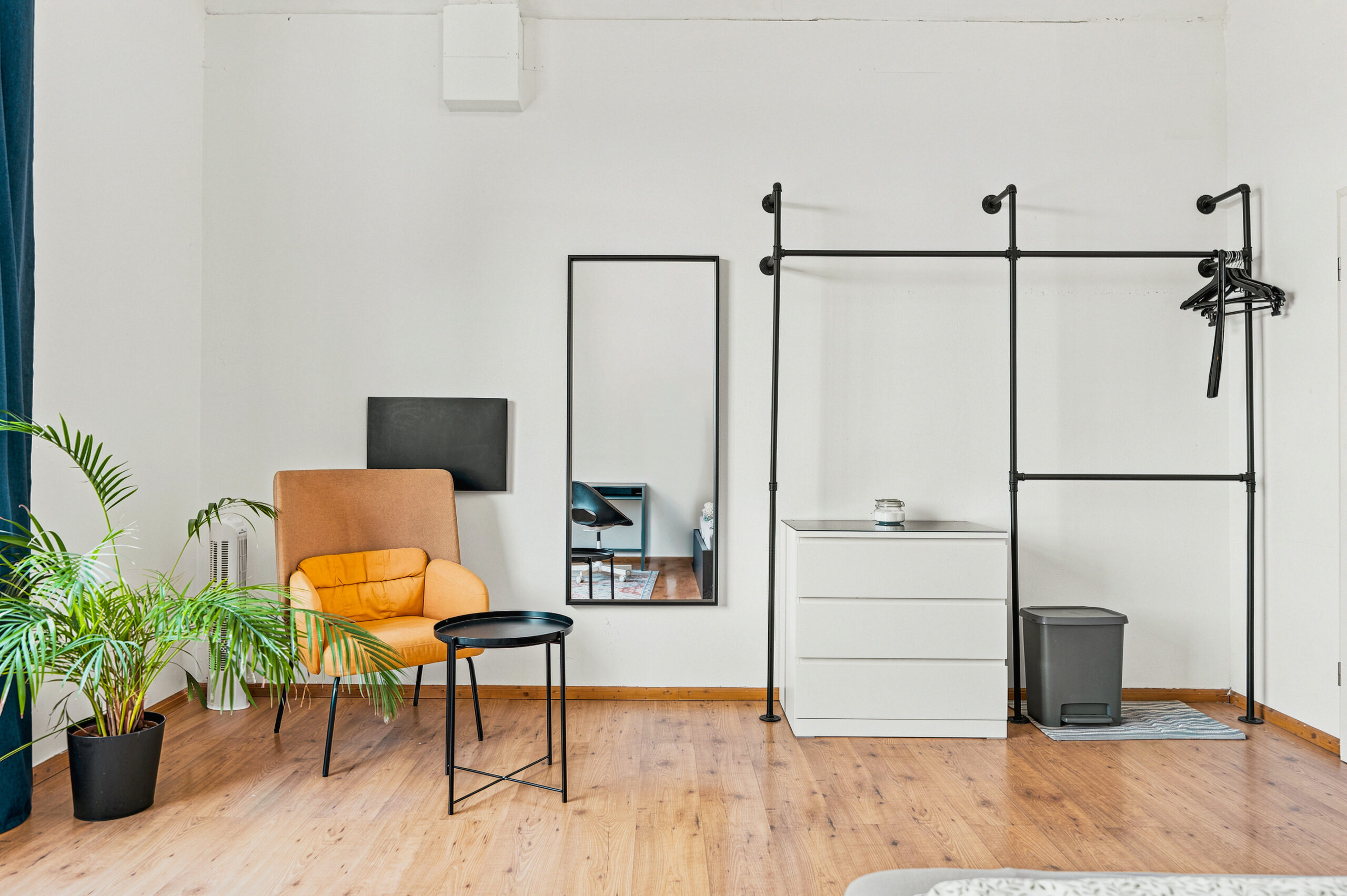 Bedroom with orange chair, mirrors, and wooden flooring.
