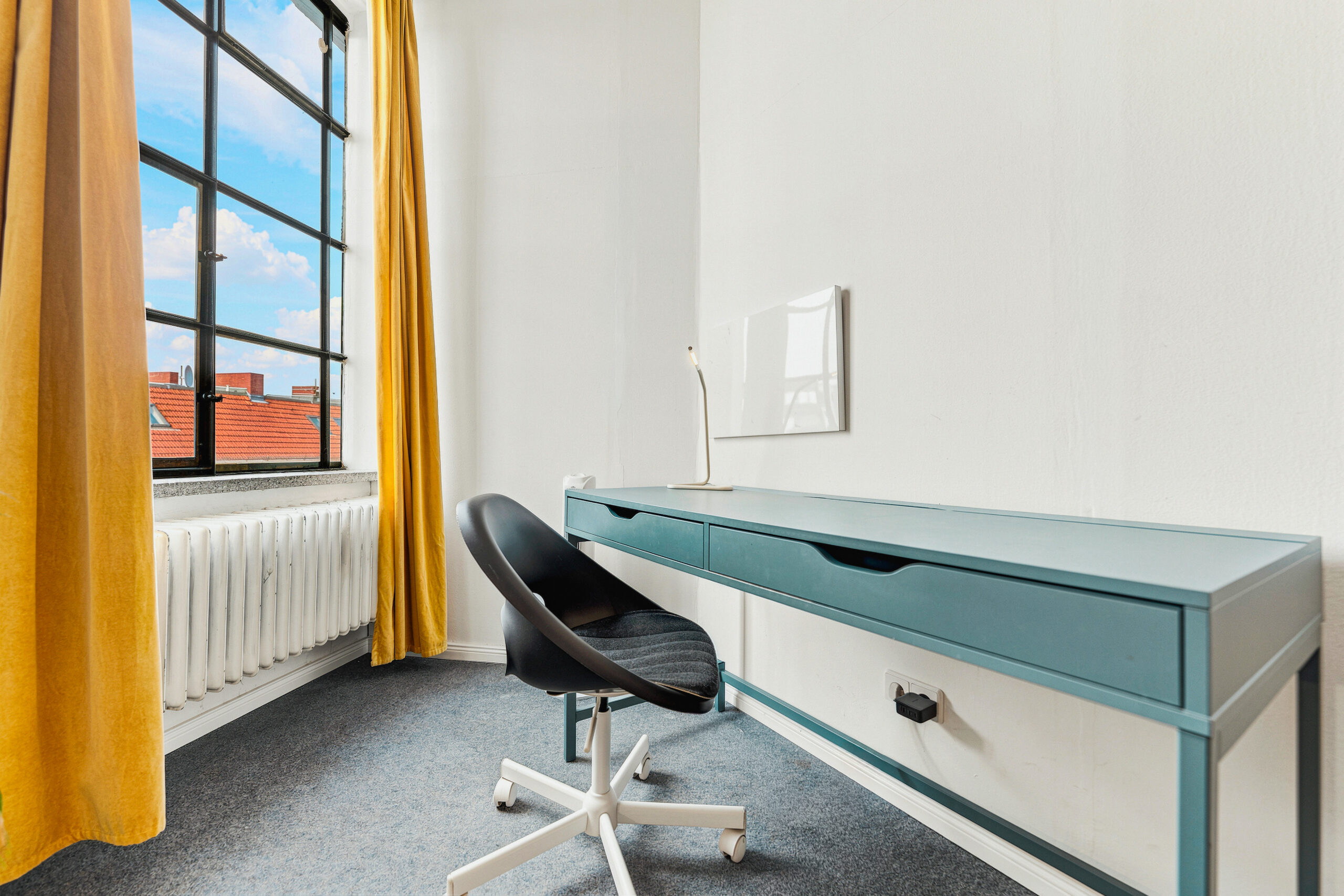 Bedroom workspace with blue desk, office chair, and window light
