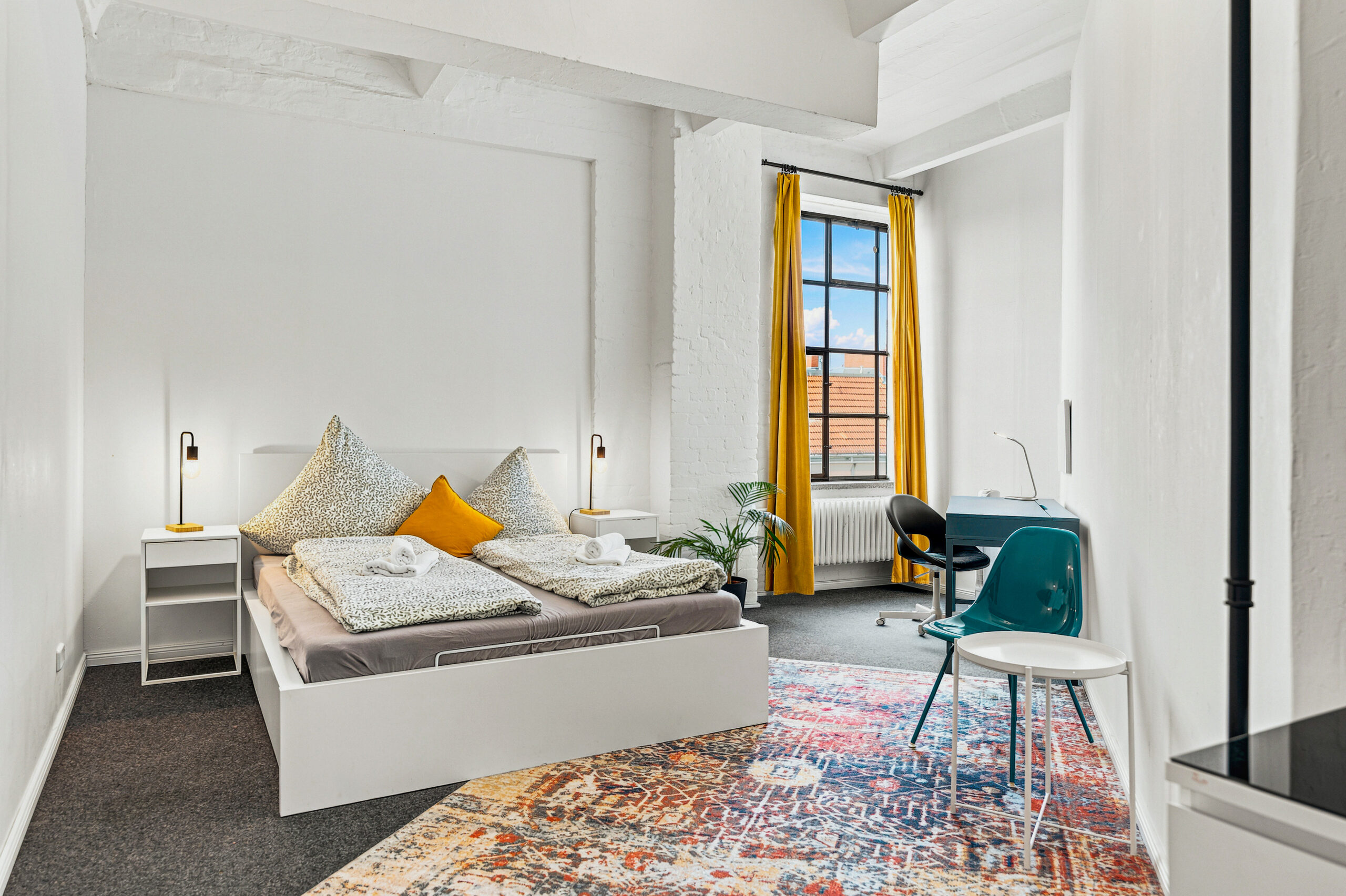 Modern bedroom with white bed, orange chair, and yellow-framed window