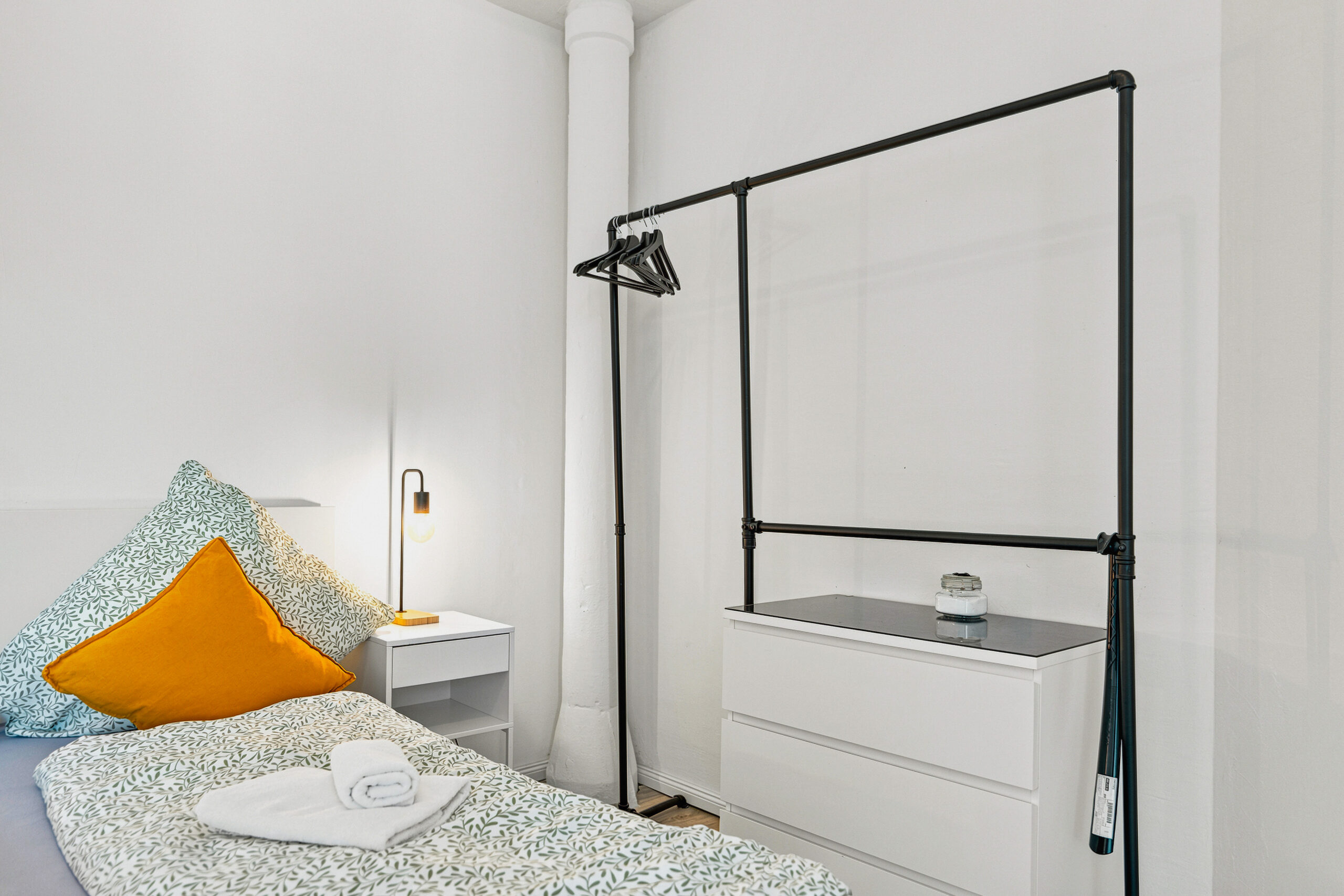 Minimalist bedroom corner with bed, yellow pillow, and black frame