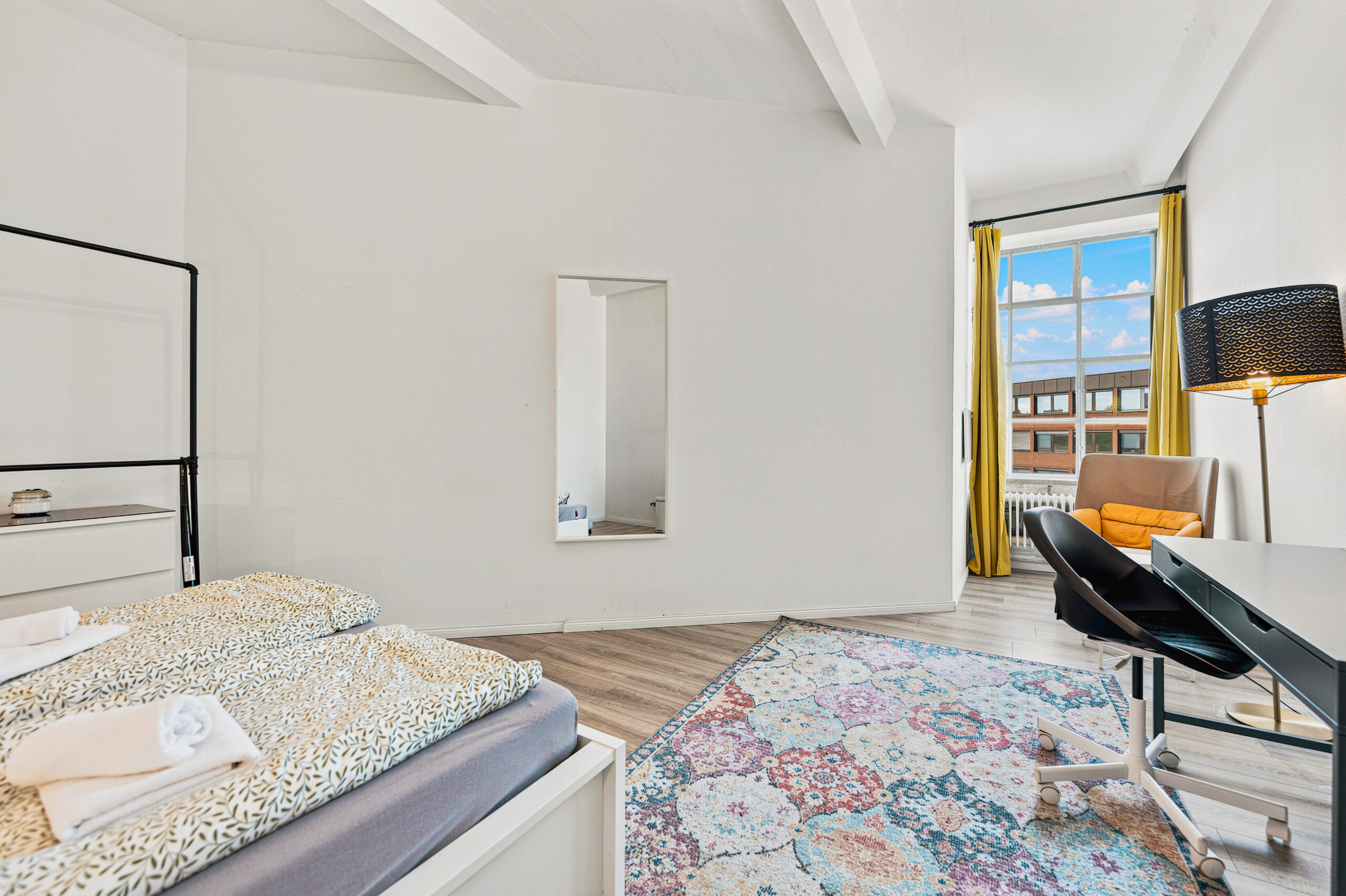 Spacious bedroom with two beds, desk, and city view window