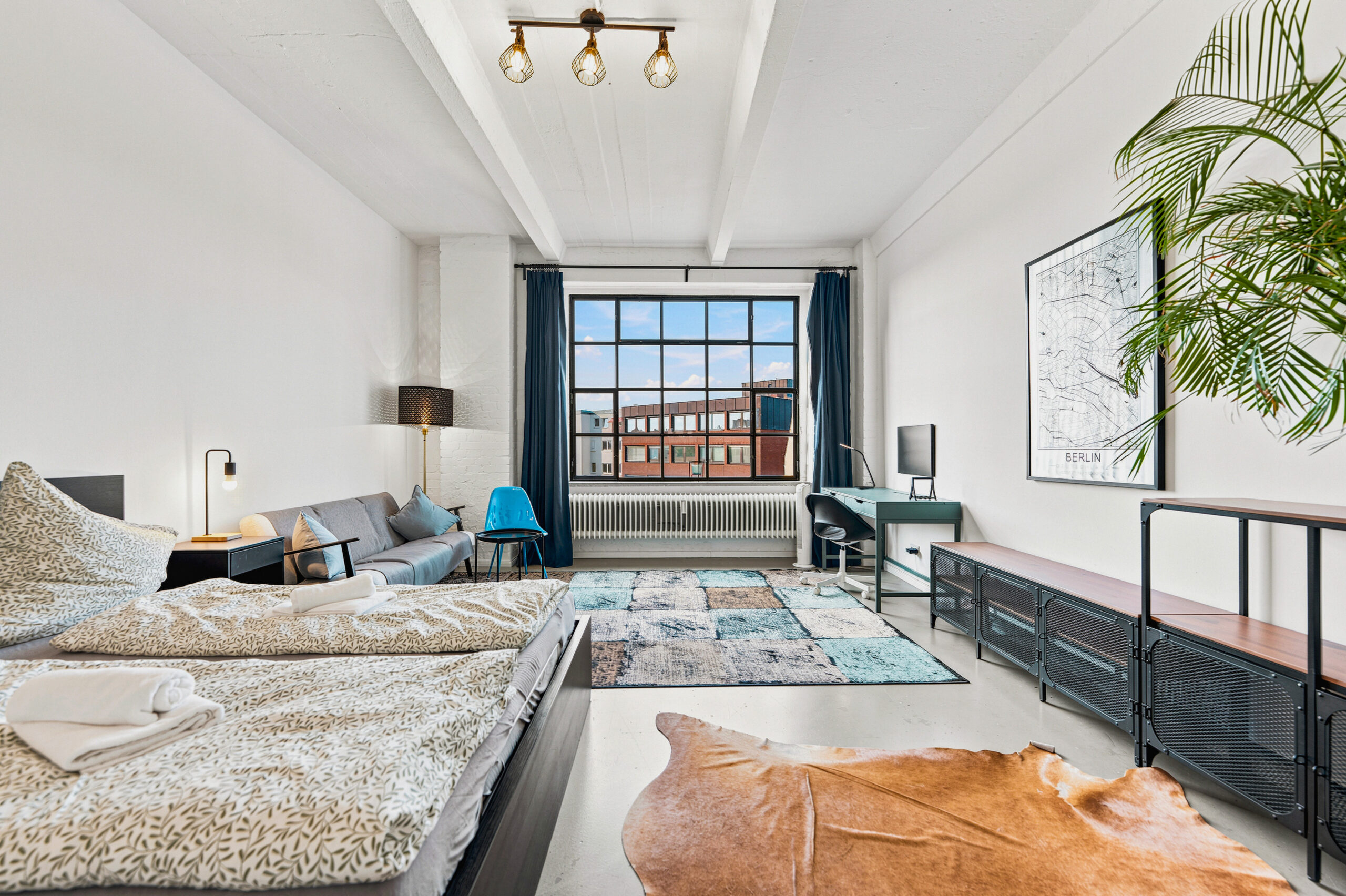 Airy bedroom with two beds, large windows, and turquoise accents